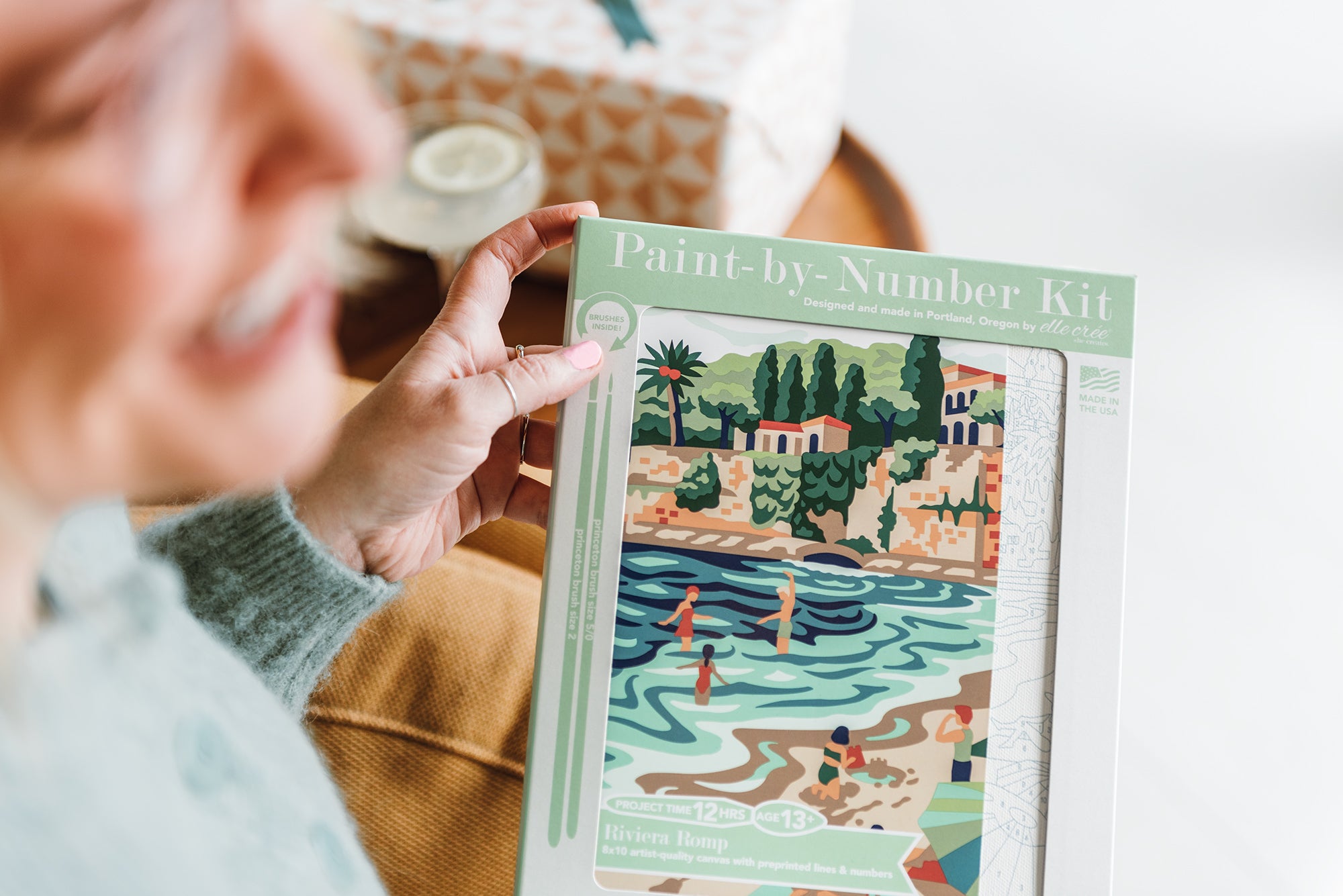 Riviera Romp paint-by-number kit held in a woman's hand's.