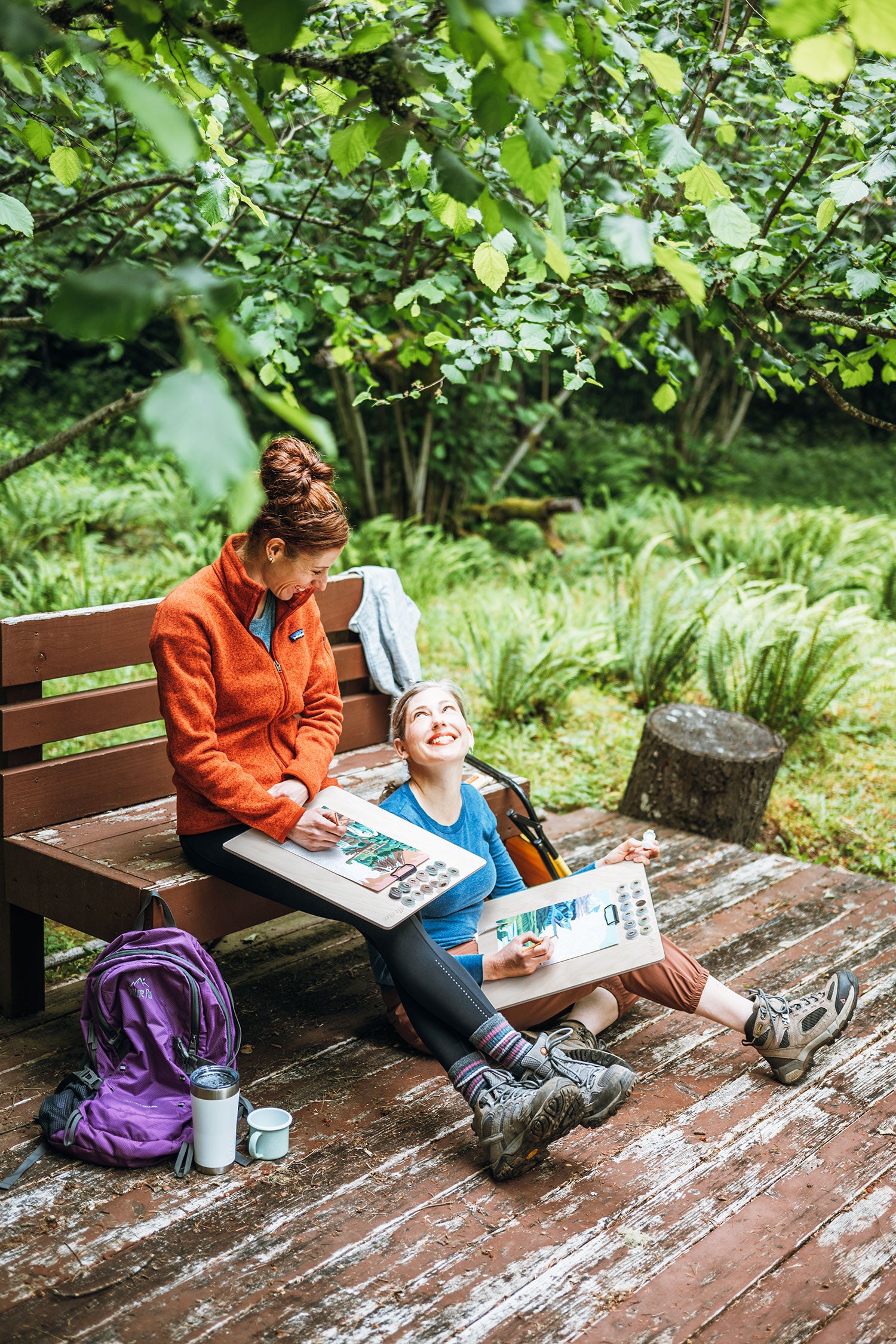 Two people sitting on a wooden bench in a forest, painting National Park paint-by-number kits from Elle Crée.