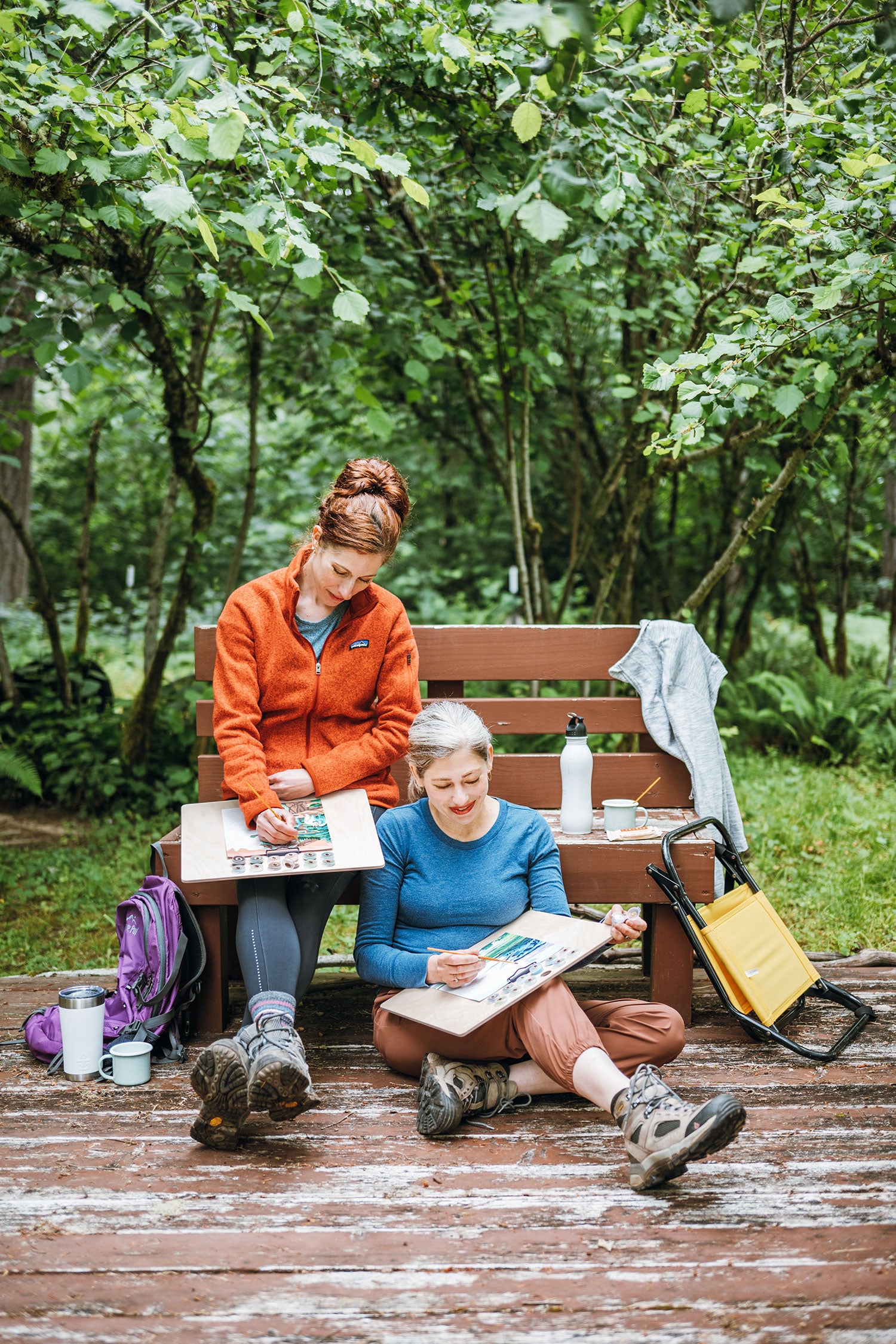 Two people sitting on a wooden bench in a forest, painting National Park paint-by-number kits from Elle Crée.