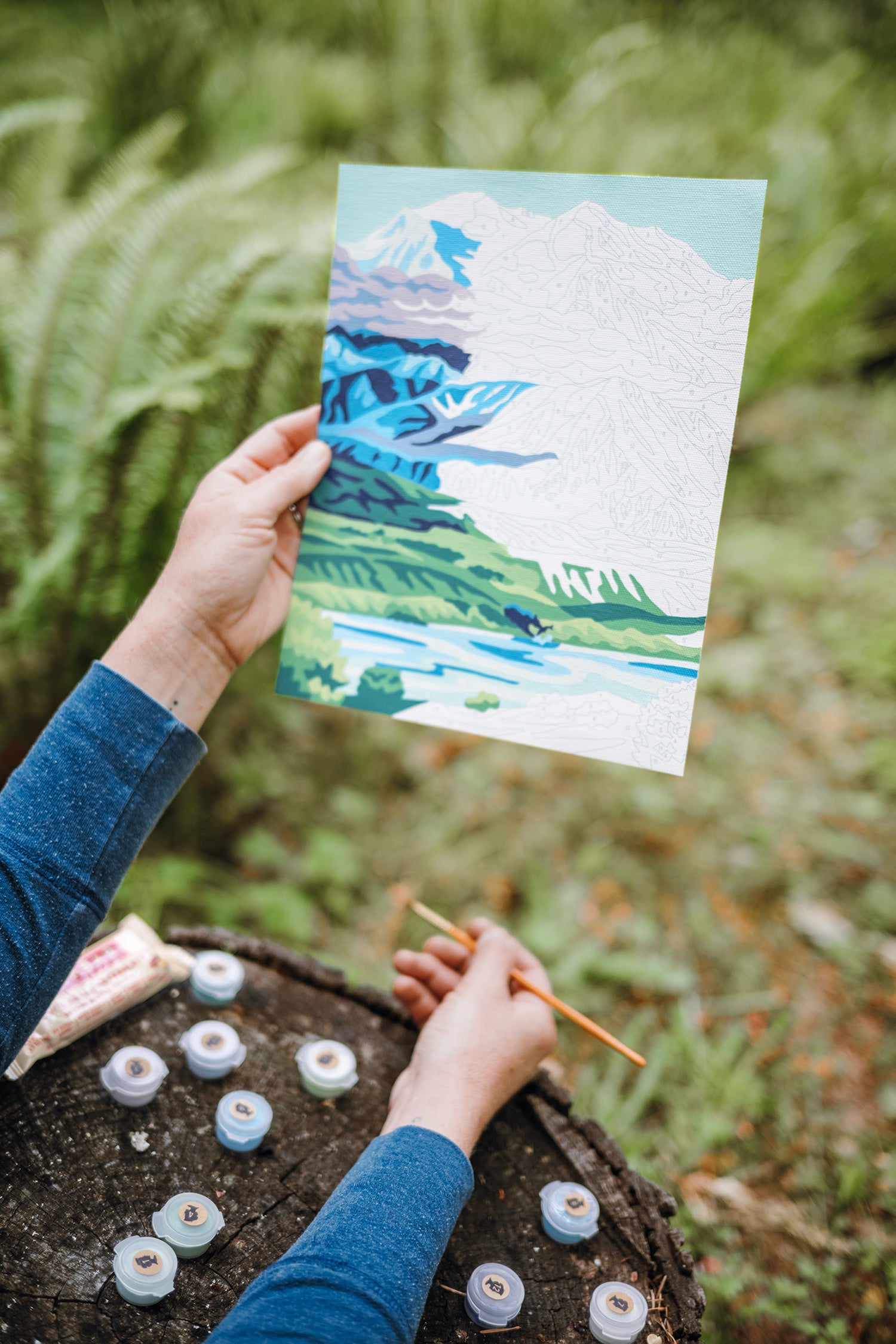 Person holding a half-finished painting of a scene from Denali National park paint-by-number kit.