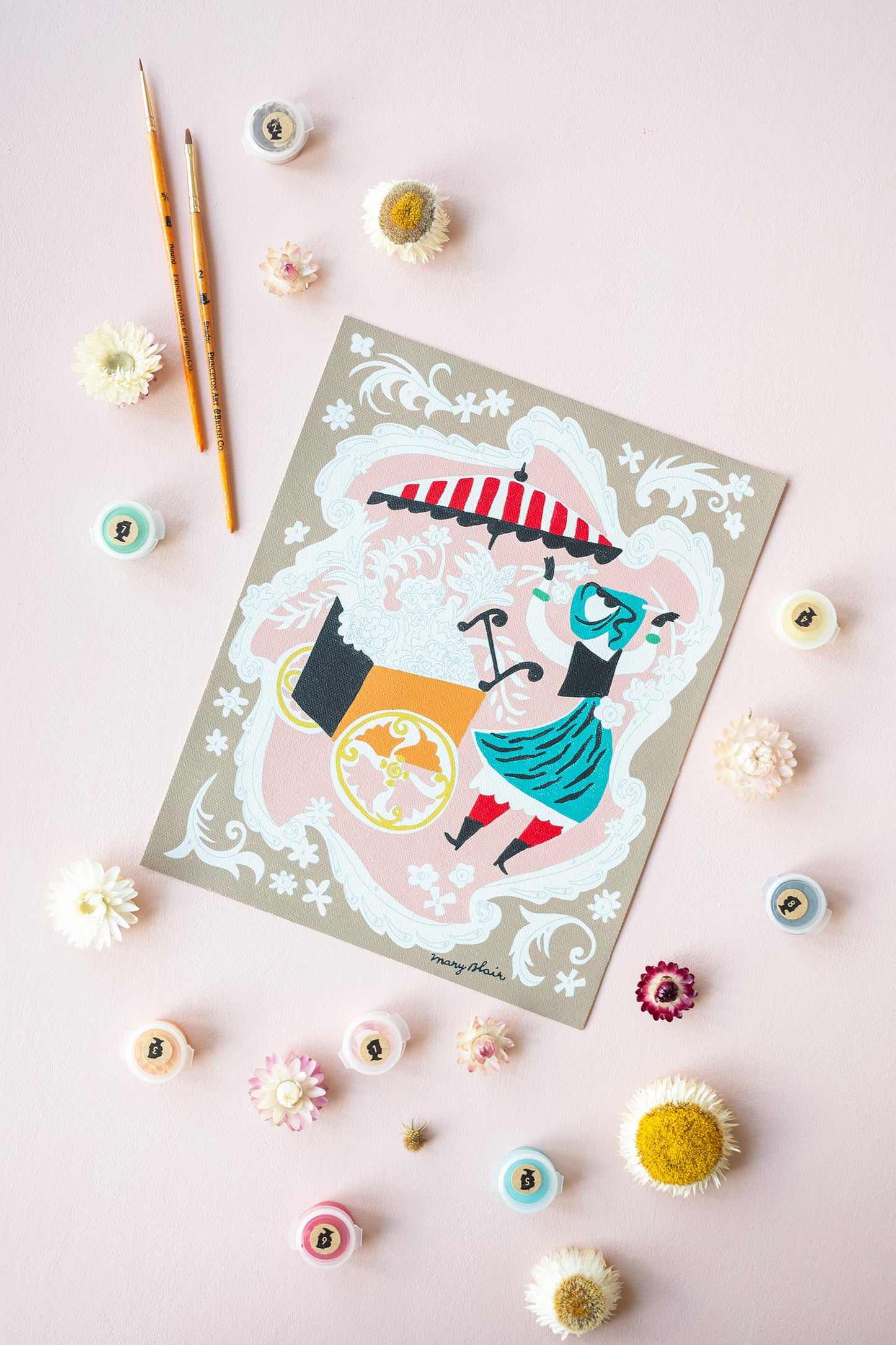 Mary Blair’s Petal Peddler paint-by-number kit in progress with flower cart scene, paint pots, brushes, and dried flowers on pink background.