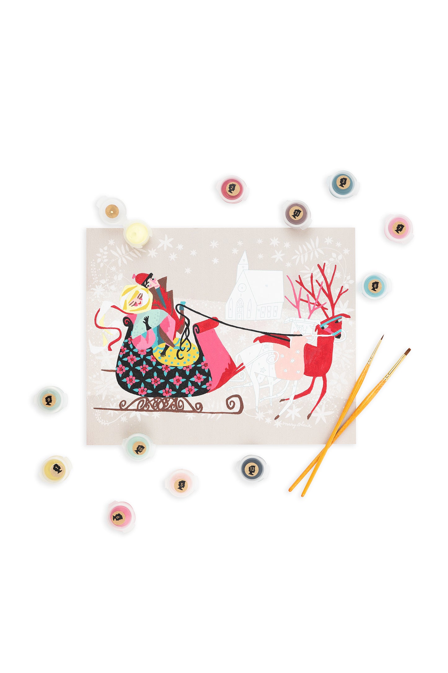 Mary Blair’s Winter Sleigh paint-by-number kit with pink reindeer, bundled couple, church scene, paint pots, and brushes on white background.