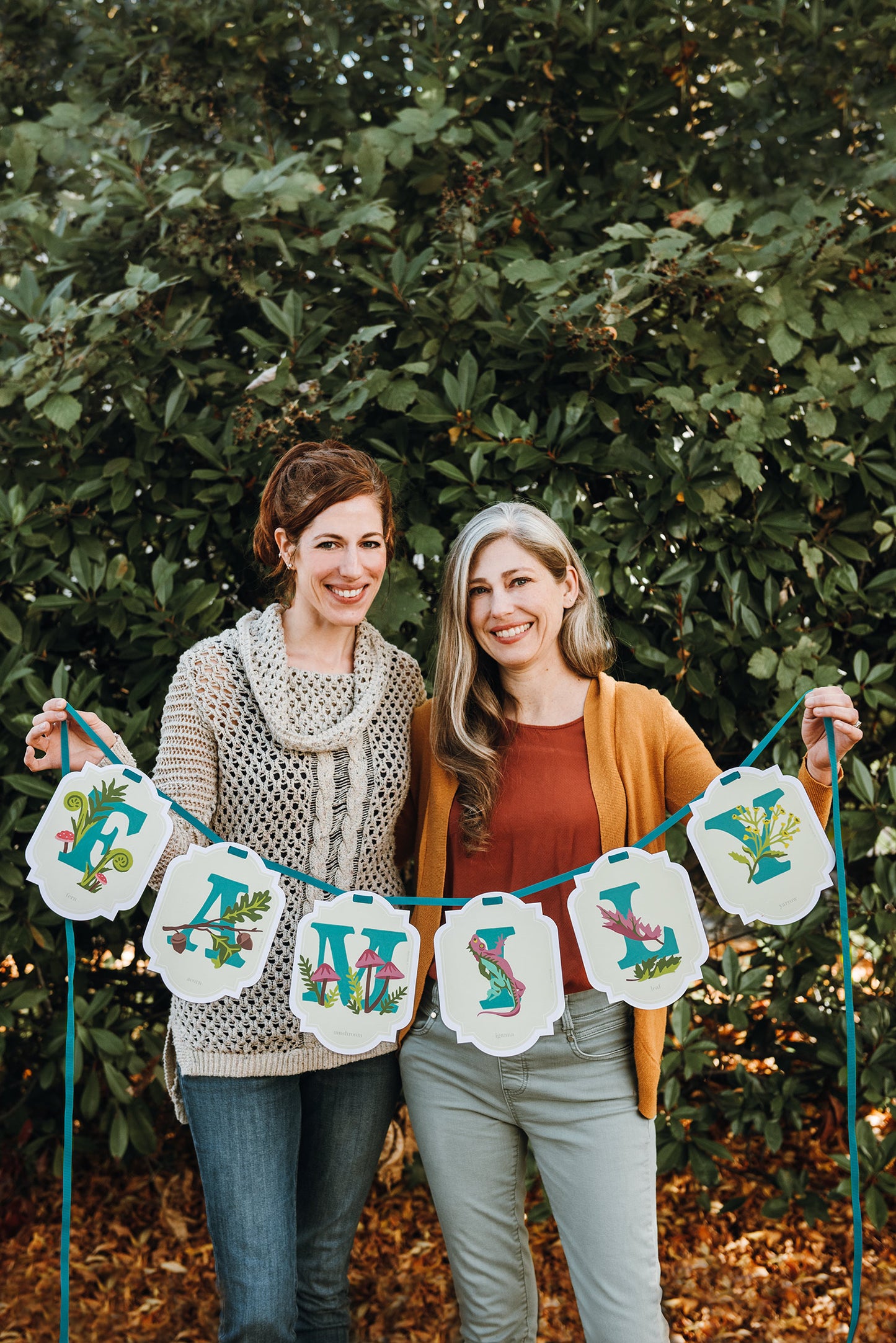 Two women holding up a fully painted paint-by-number banner kit that reads "Family."
