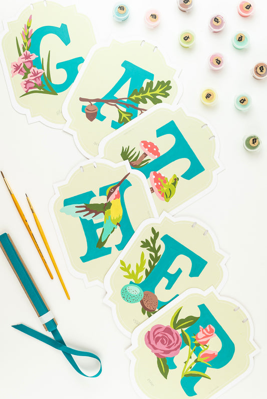 GATHER paint-by-number. banner kit, fully painted and displayed on a white background surrounded by paint pots, brushes, and blue ribbon.