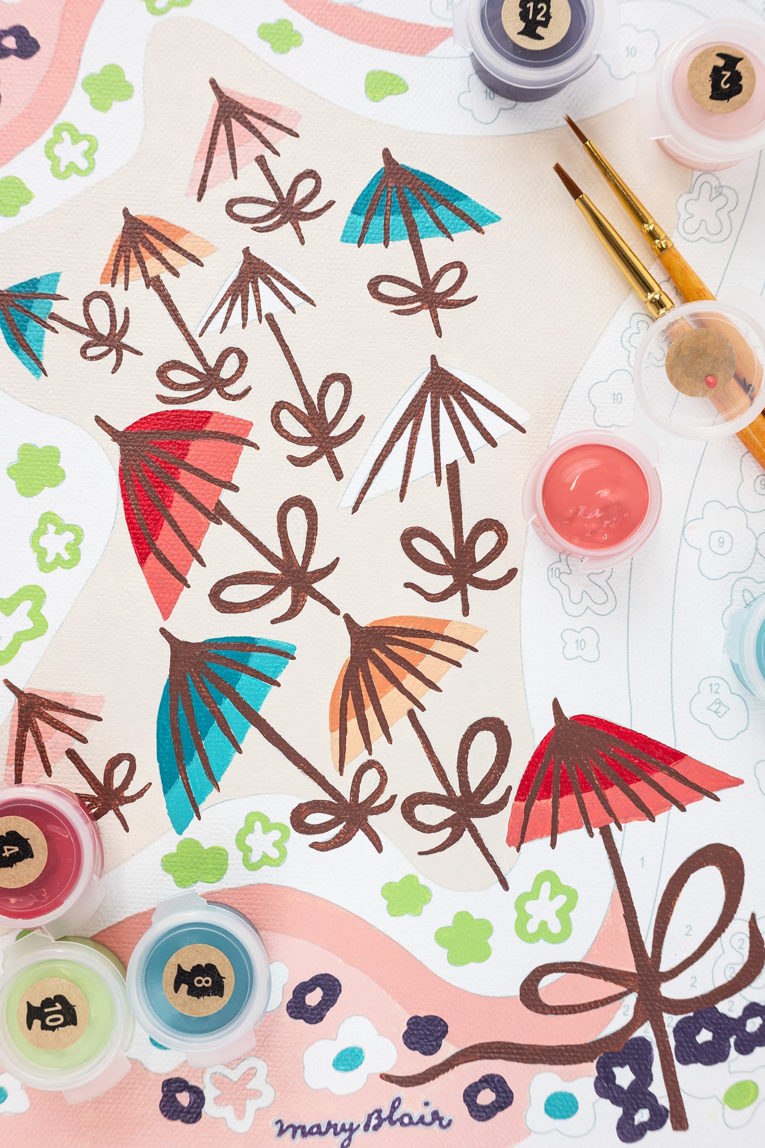 Close-up of a paint-by-number kit depicting colorful umbrellas and decorative elements on a white background with the 'Mary Blair' signature.