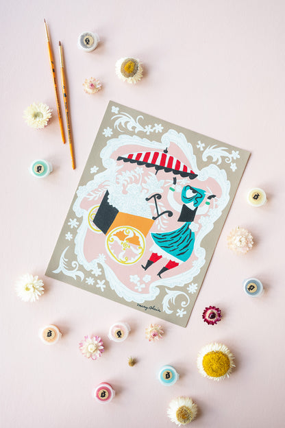 Mary Blair’s Petal Peddler paint-by-number kit in progress with flower cart scene, paint pots, brushes, and dried flowers on pink background.