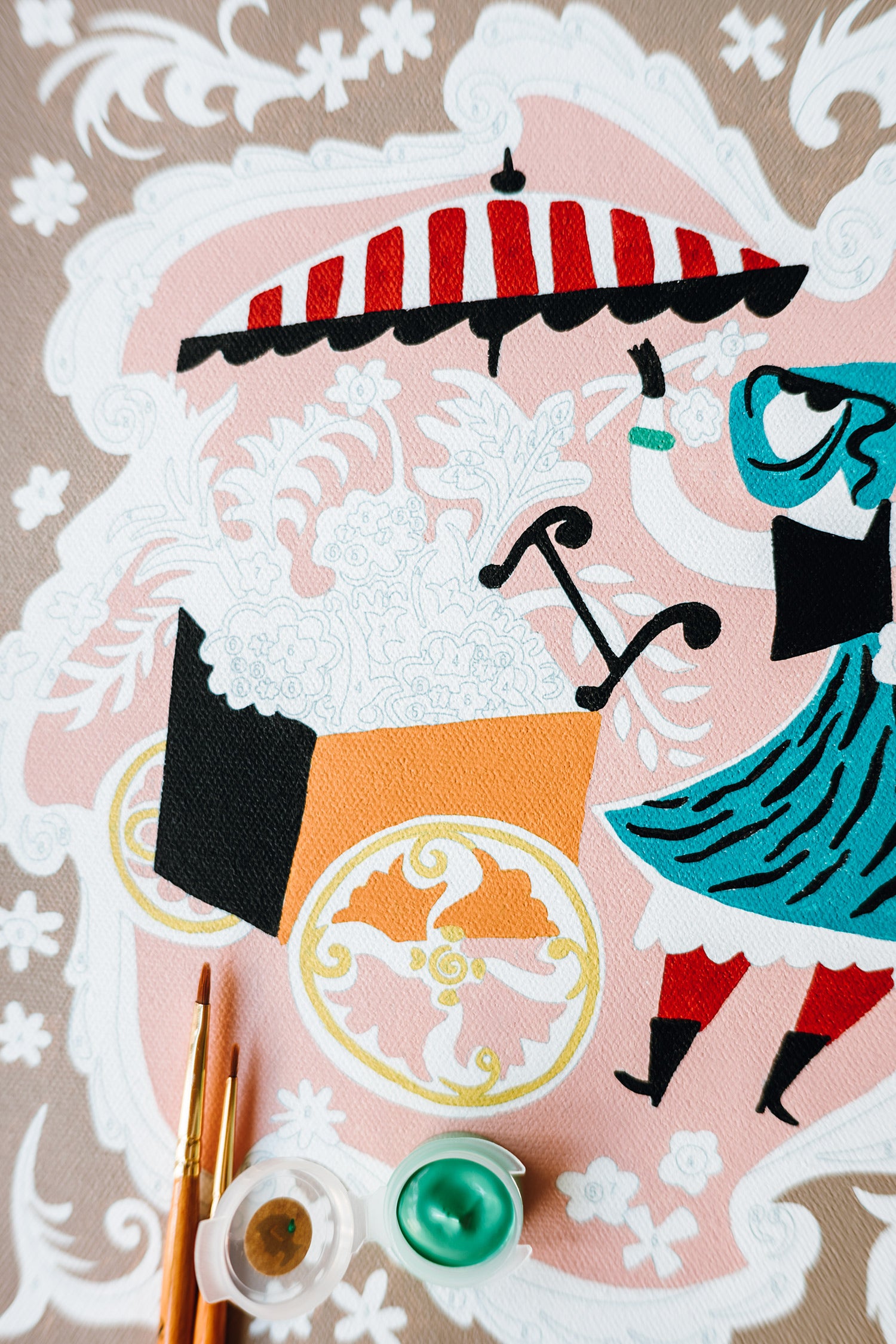 Close-up of Mary Blair’s Petal Peddler paint-by-number kit showing flower cart, striped umbrella, paintbrushes, and green paint pot.