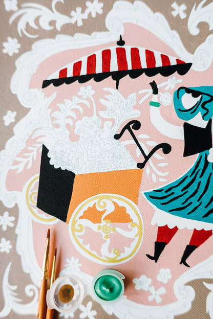 Close-up of Mary Blair’s Petal Peddler paint-by-number kit showing flower cart, striped umbrella, paintbrushes, and green paint pot.