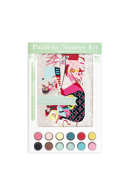 Mary Blair’s Winter Sleigh Ride paint-by-number kit packaging with bundled couple, pink reindeer, snowy scene, 12 paint pots, and brushes.