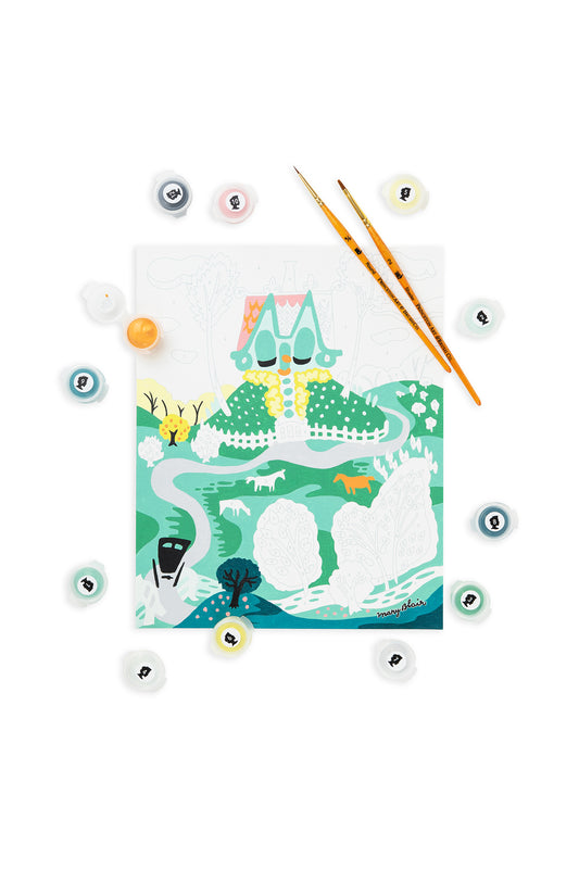 Mary Blair Little House paint-by-number kit showing a whimsical cottage on a hill with winding road, trees, animals, and paint pots arranged around the canvas.
