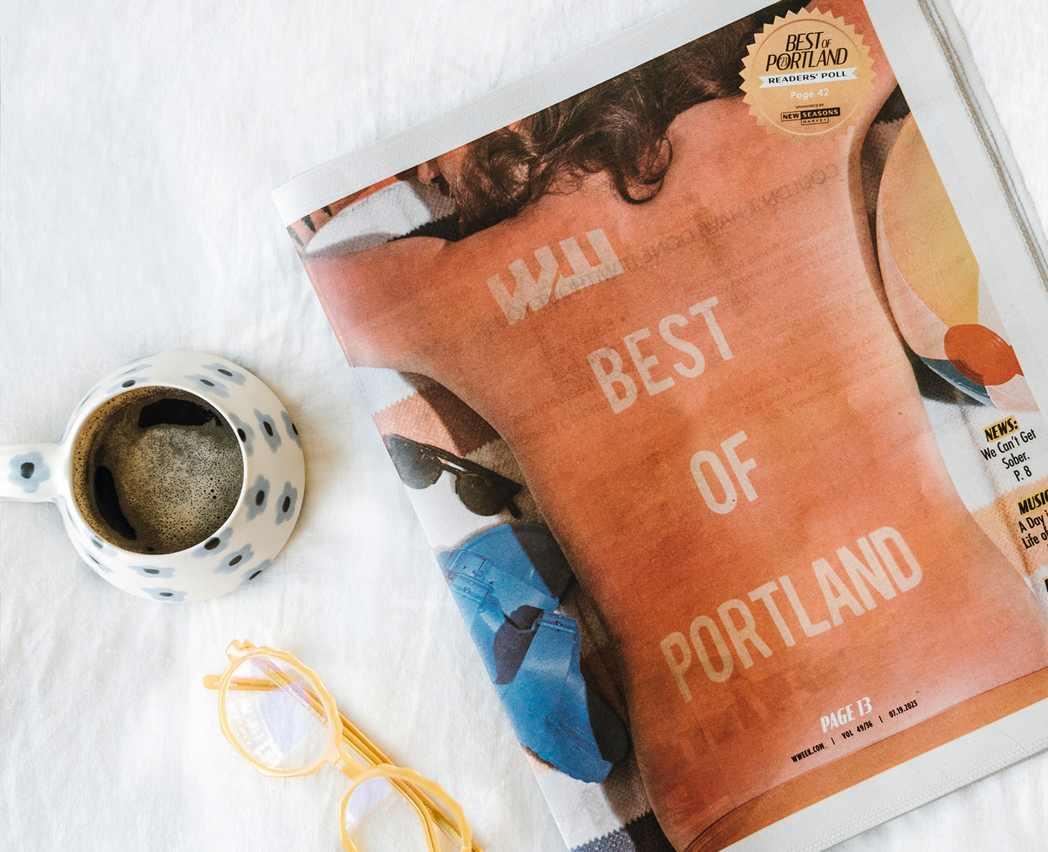 Willamette Week's Best of Portland Issue on a white blanket next to a mug of coffee and reading glasses.